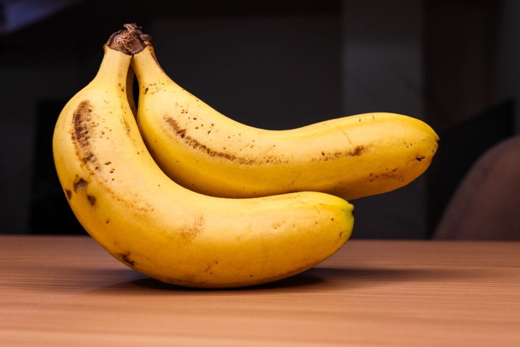 Two ripe bananas on a wooden table, showcasing their bright yellow color and natural texture.